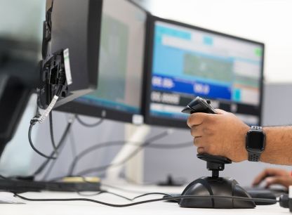 A hand using a joystick on a computer with three screens
