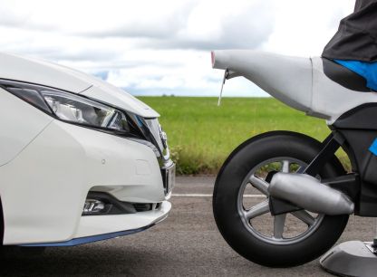 An AB Dynamics testing dummy motorbike and a white car close behind it on a testing track