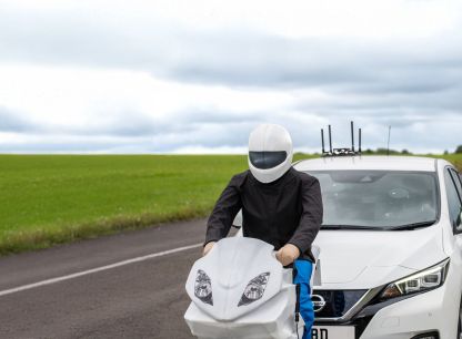 A white car close behind an AB Dynamics test dummy on a motorbike